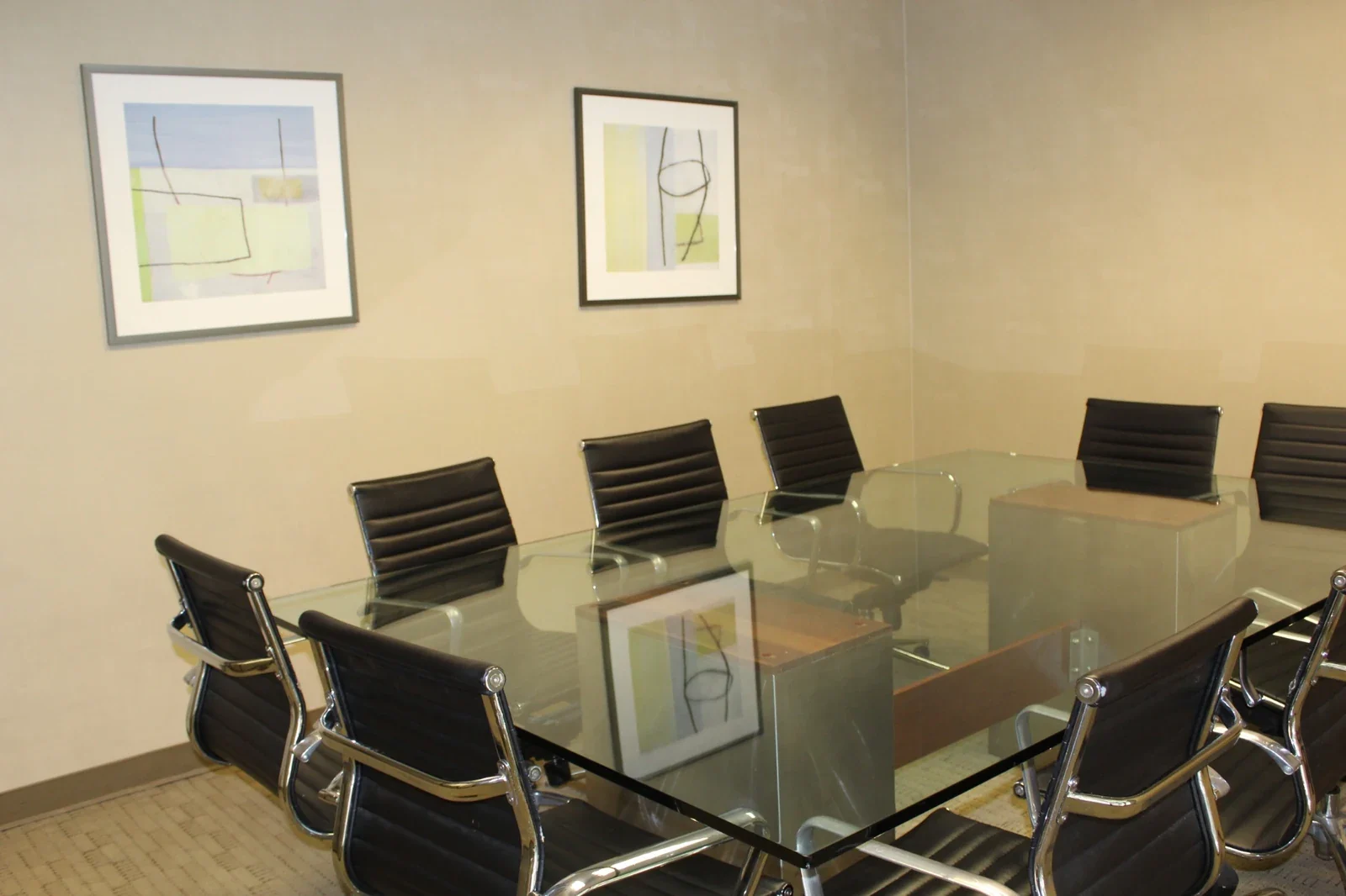Mesa de reuniones con sillas negras y obras decorativas en la pared.