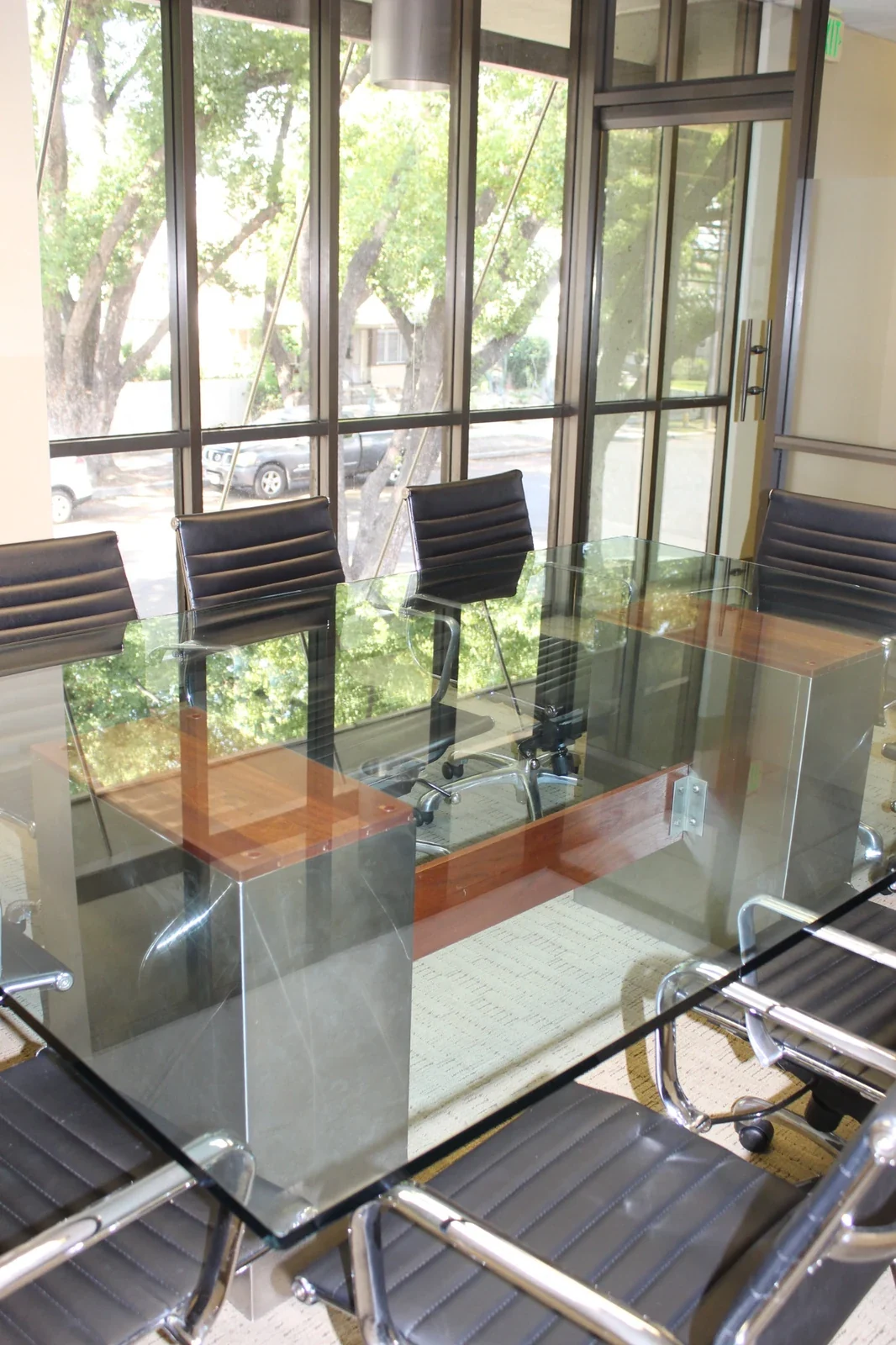 Glass meeting table with black ribbed chairs beside tall windows and trees.