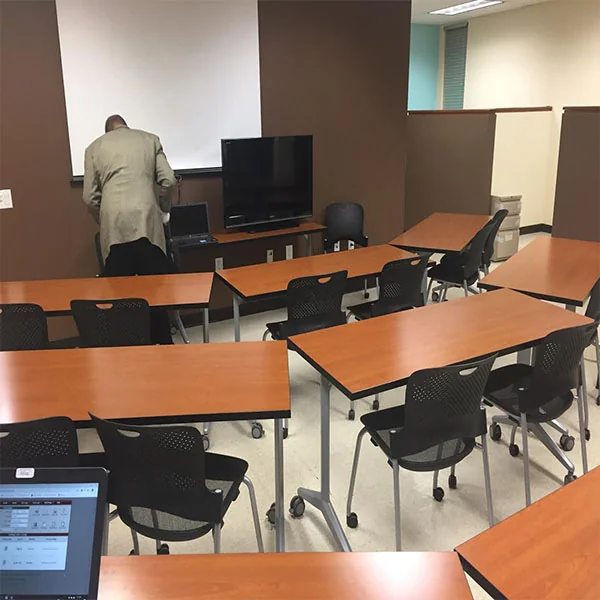Training tables facing a monitor; one person near the front is seen from behind.